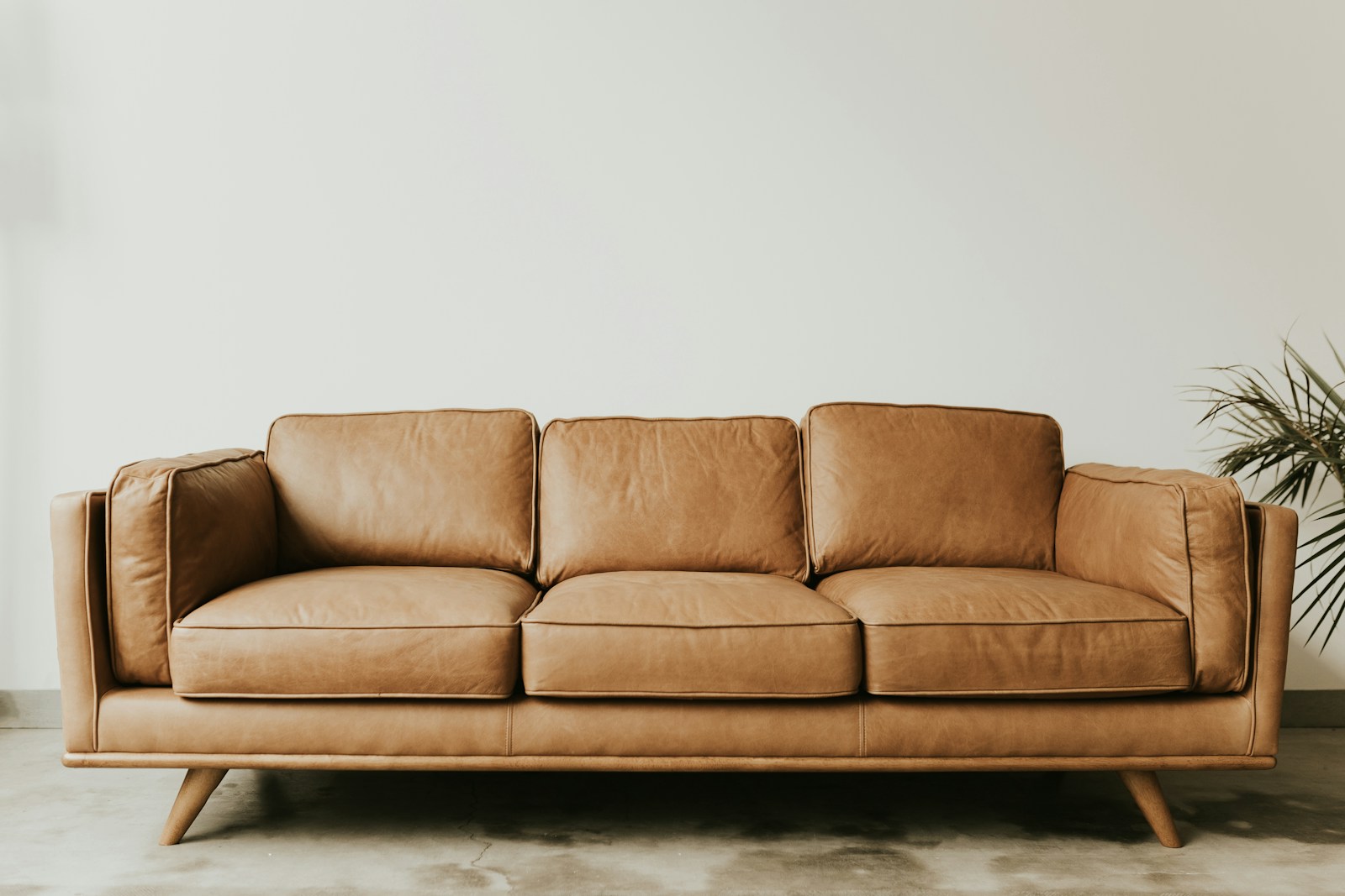 Tan three-seater sofa with three back cushions and tapered legs